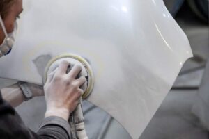 A person examining damage to the front of a silver car on a residential street.
