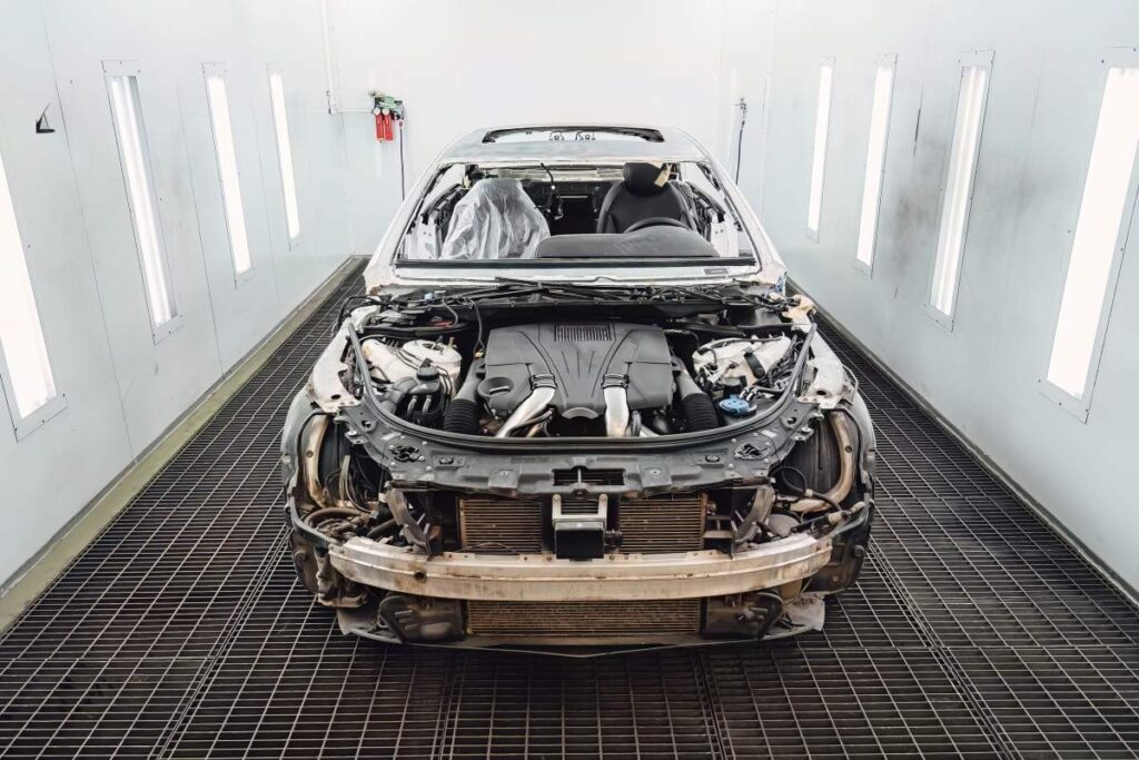 Technicians inspecting a vehicle with visible collision damage in a repair garage during winter.