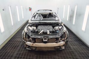 Technicians inspecting a vehicle with visible collision damage in a repair garage during winter.