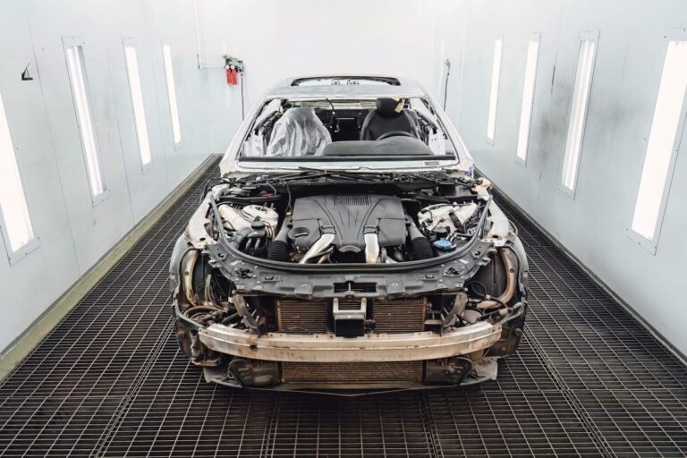 Technicians inspecting a vehicle with visible collision damage in a repair garage during winter.